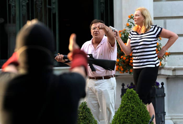 A man and woman, carrying a large gun and pistol, respectively, shout at protesters from a distance