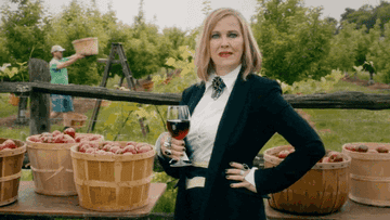 Moira Rose from Schitt&#x27;s Creek holding a glass of red wine in a suit on a farm