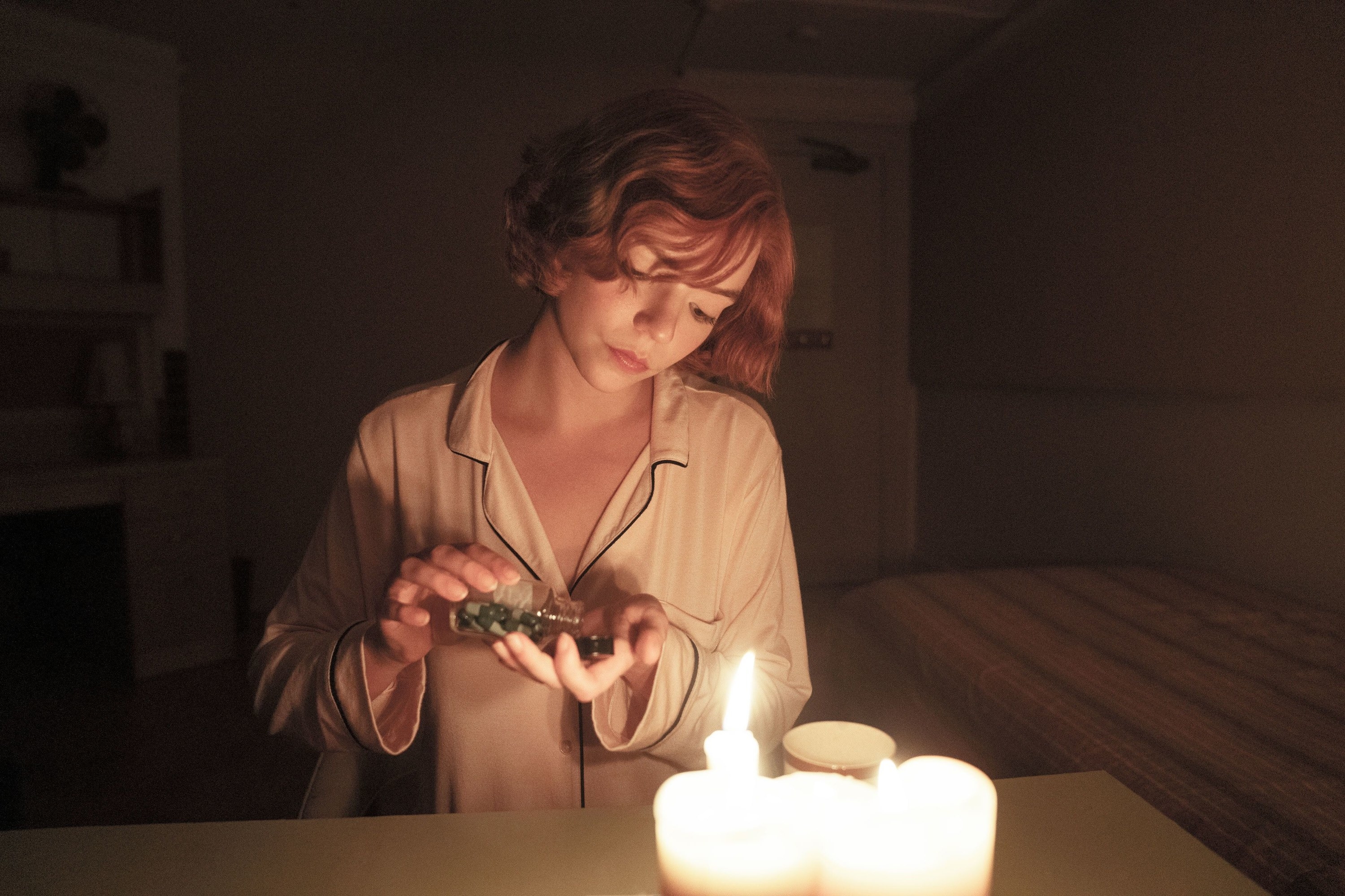 Woman taking some pills out of a bottle by candlelight