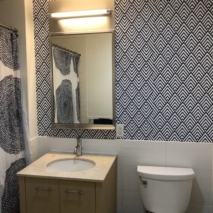 A reviewer image of a bathroom that has been decorated with the wall paper, which is white with blue overlapping diamond outlines