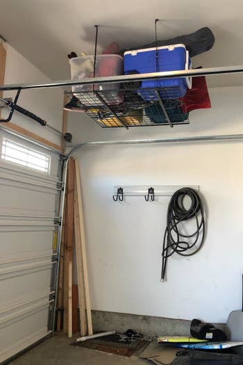 a reviewer photo of a garage with a wire shelf hanging from the ceiling with tubs on it 