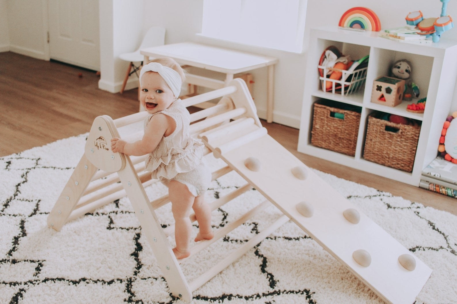 baby standing on the wooden climber with different rugs for stepping and a slide