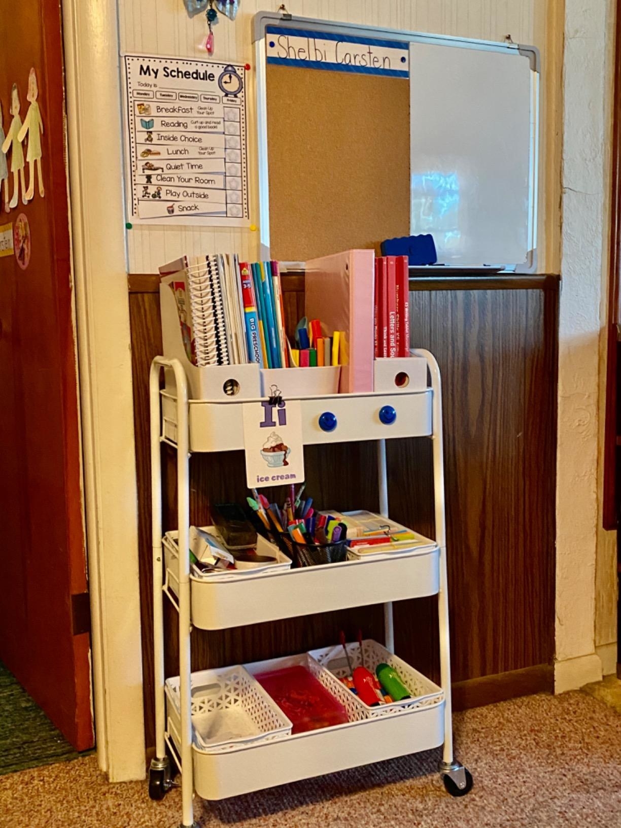 reviewer photo of a white three-tiered metal utility cart with wheels holding school supplies
