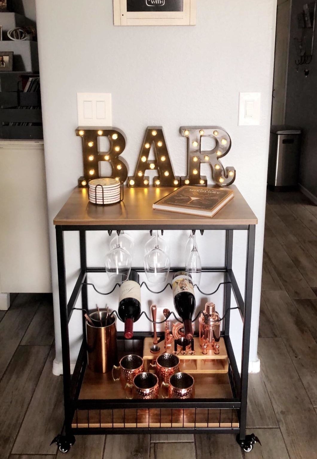 reviewer photo of a bar cart with wood-colored top and metal frame and legs, with bar accessories on top