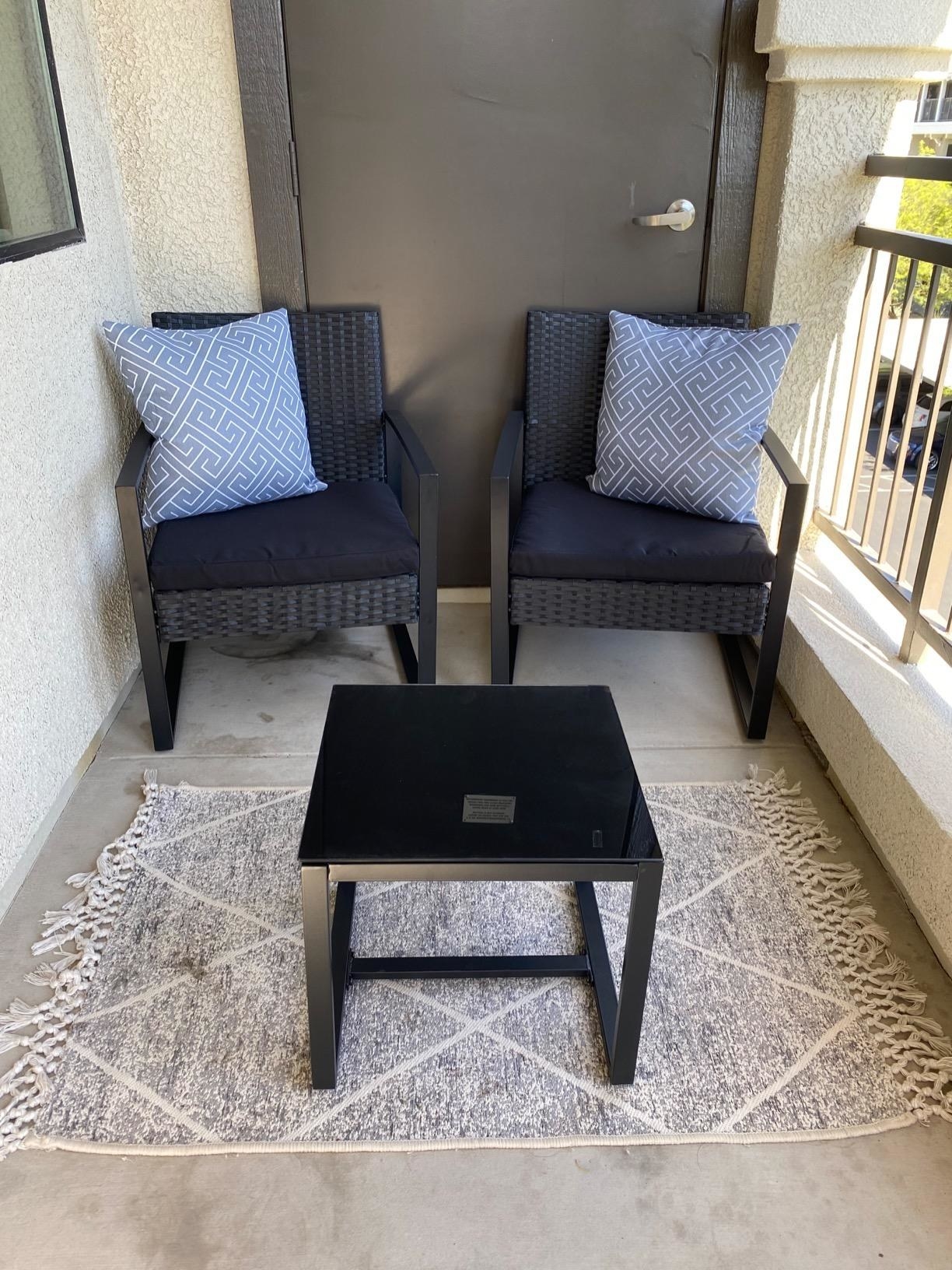reviewer photo of a three-piece patio set including two rattan chairs with black cushions and a small table with glass top