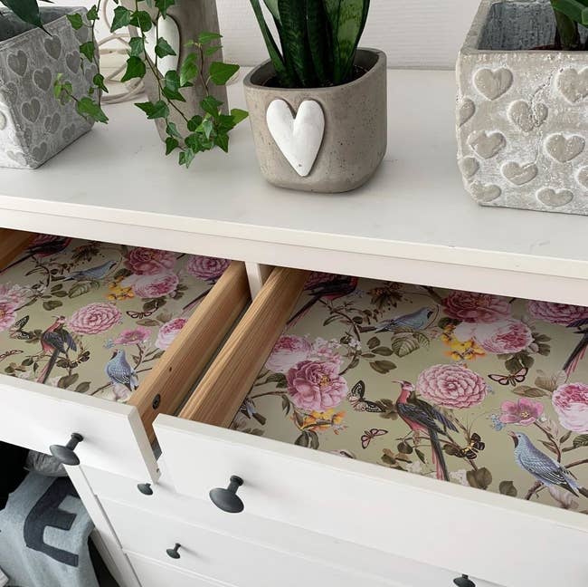 A reviewer's partially open drawer revealing a floral and bird design liner inside a white dresser with silver knobs