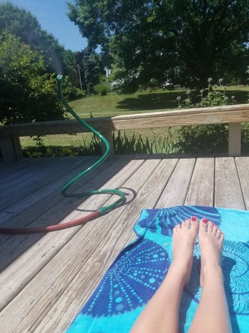 reviewer photo of a green mister outside by someone sunbathing