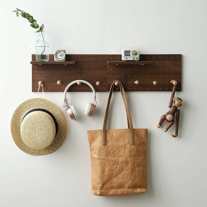 The wall organizer with eight hooks and two shelves holding a hat, a tote bag and more