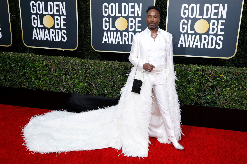 Billy Porter posing on the red carpet in a long, white, feathered cape