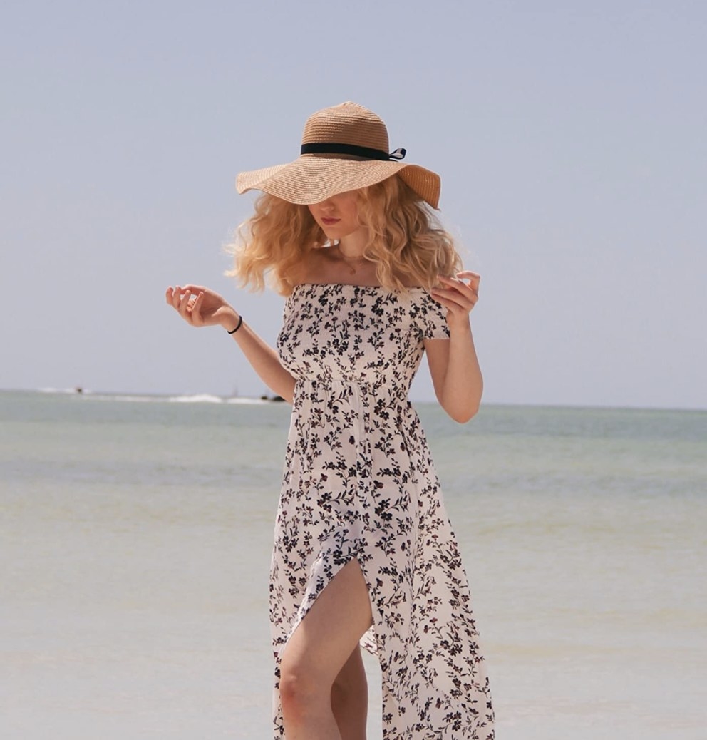 A person wearing a white and black maxi dress and sun hat
