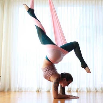 Person doing yoga pose with arms on the ground and legs suspended in the air with the hanging material 