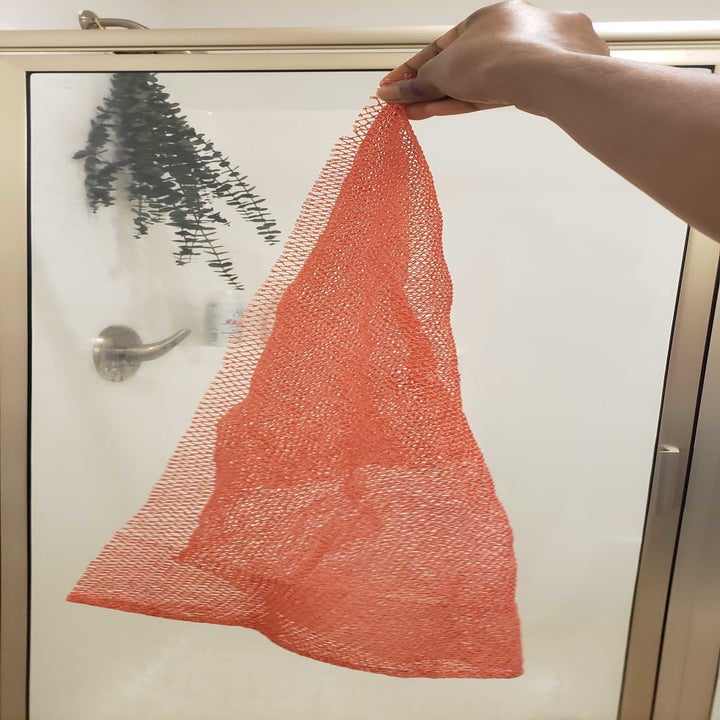 BuzzFeed editor Marquaysa Battle's hand holding the mesh body exfoliator in a dark pink color 