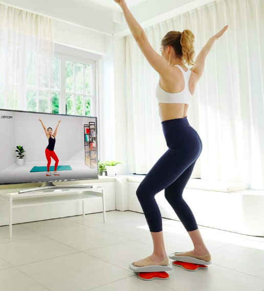 Person standing on the spinning foot pads while watching a workout class on tv