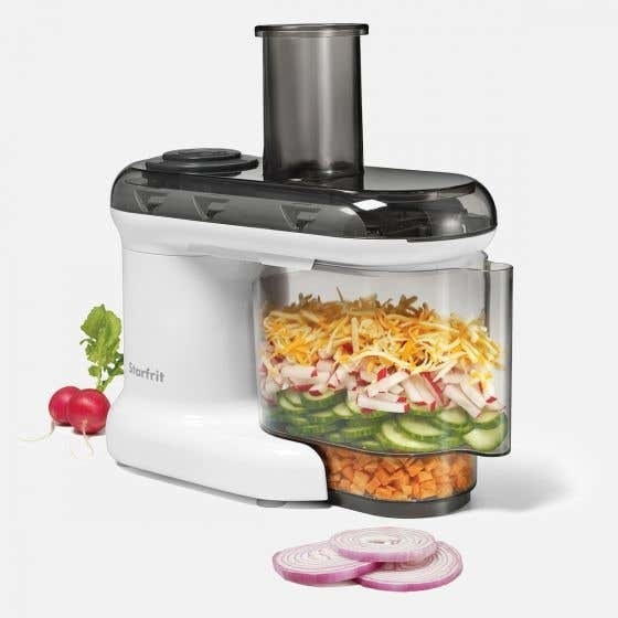 A large mandoline food processor with chopped vegetables sitting in a container beside it