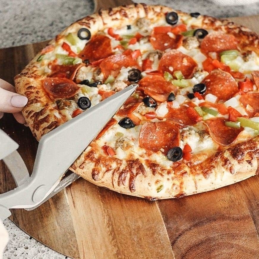 A person using giant scissors to cut through a pizza