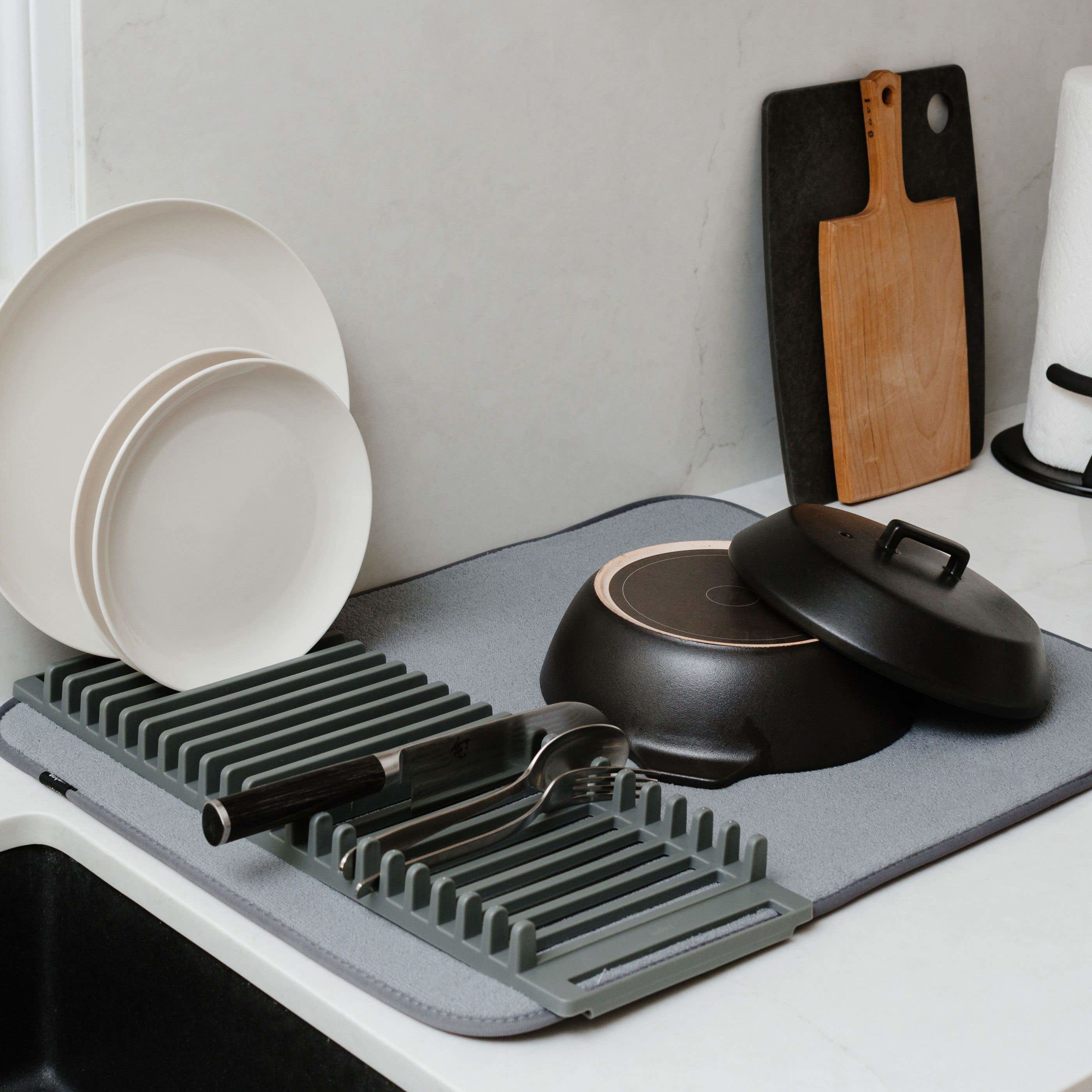 A silicone dish rack attached to a large micofibre mat that has a cup, plates and a couple of forks drying on it