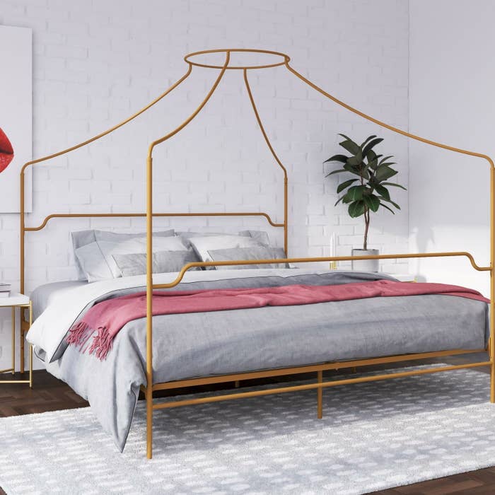 The bed frame, which has rails at headboard and footboard placement, and four canopy columns that meet in a circle over the middle of the bed, in gold