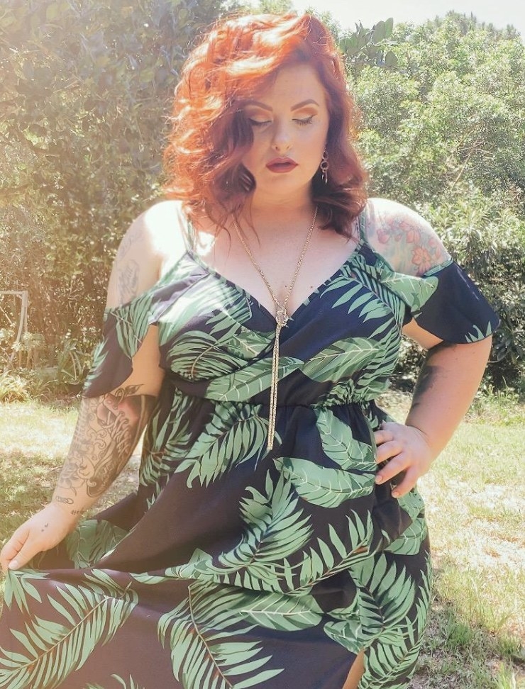 A person wearing a black cold shoulder dress with green tropical palm leaves