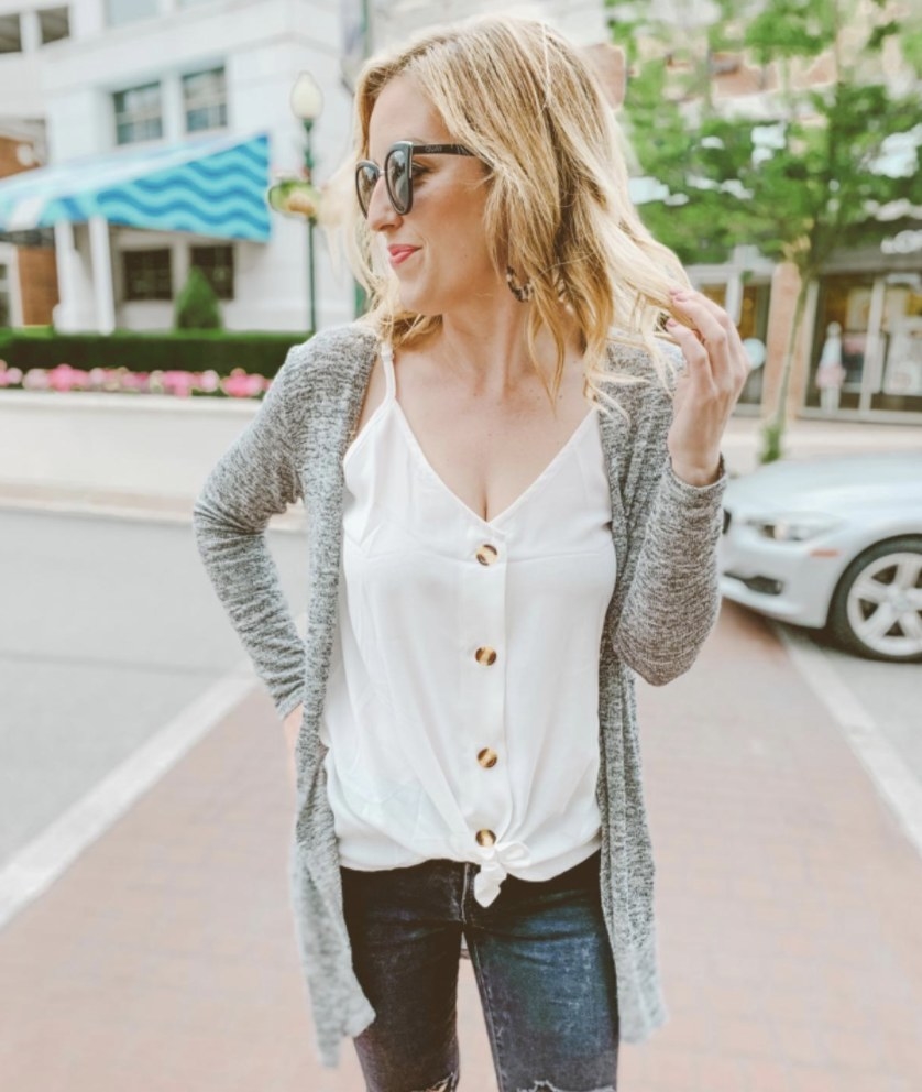 A reviewer wearing a white button-down tank, grey cardigan, and denim jeans