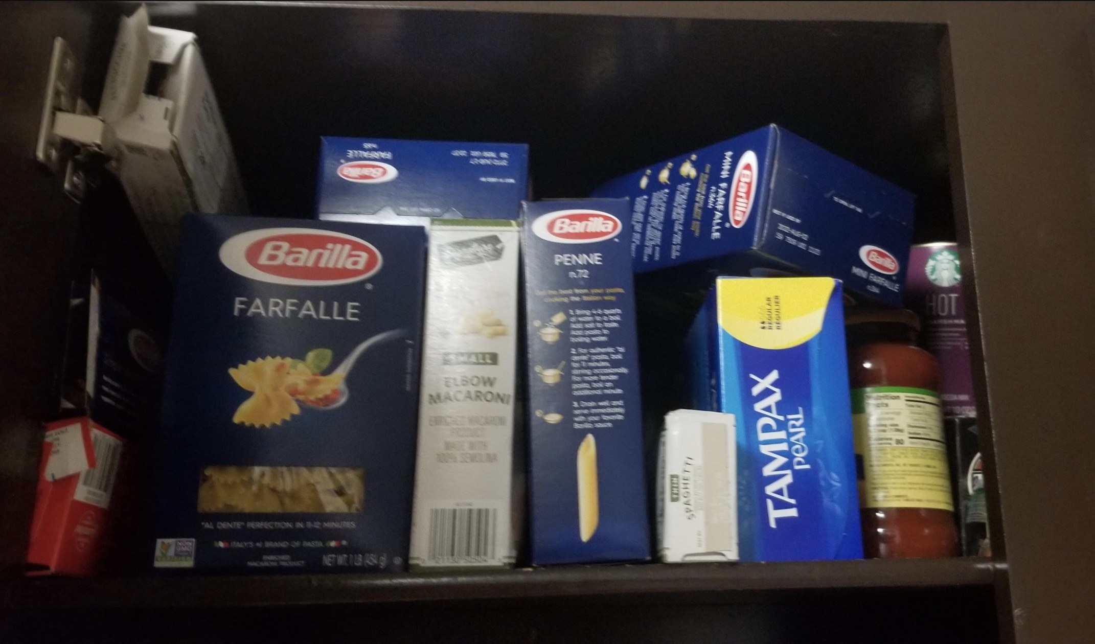 A shelf showing boxes of pasta, pasta sauce, and a box of Tampax