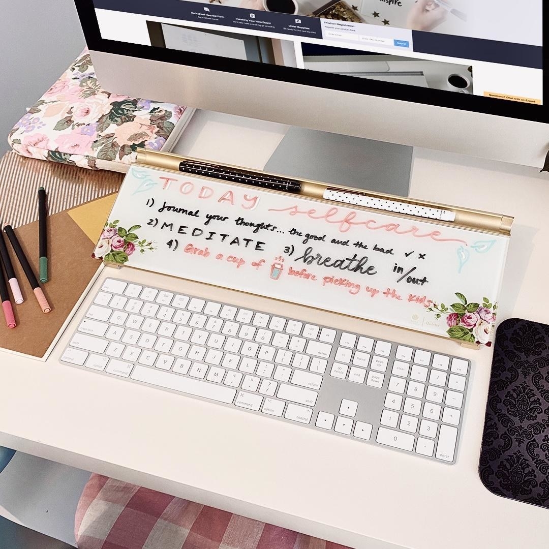 The dry erase board on a desk in front of a computer