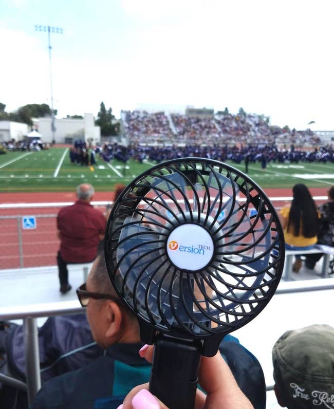 reviewer holding up a black personal fan outside