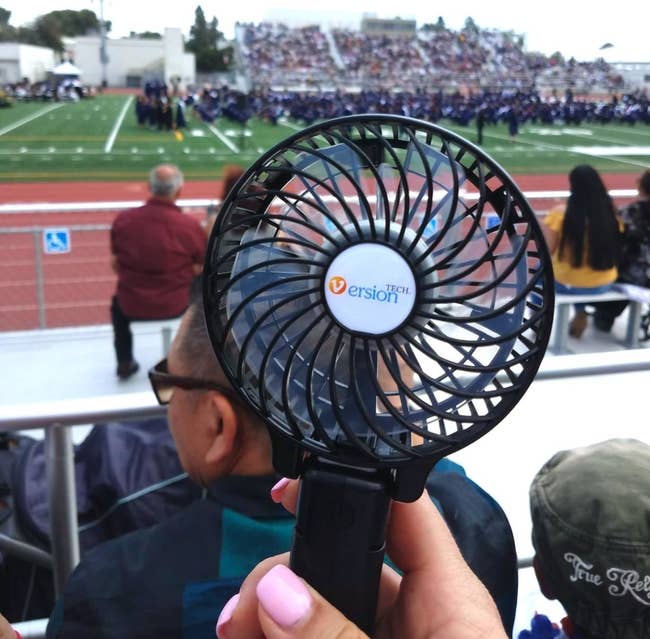 reviewer holding up a black personal fan outside