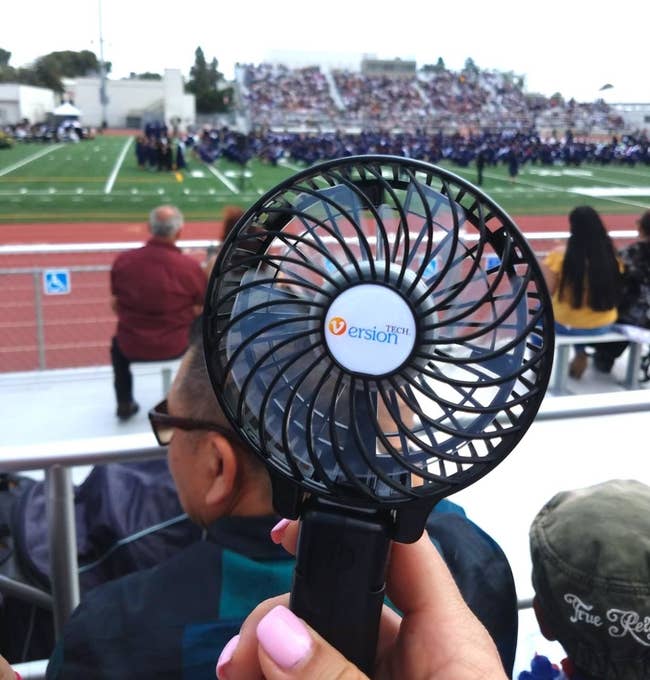 reviewer holding up a black personal fan outside