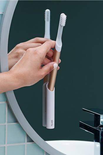 a model placing a rose gold toothbrush in a stick-on caddy