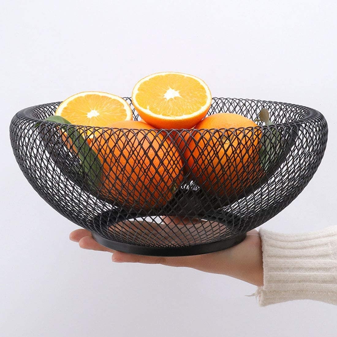 A person holding the mesh bowl with citrus fruit inside