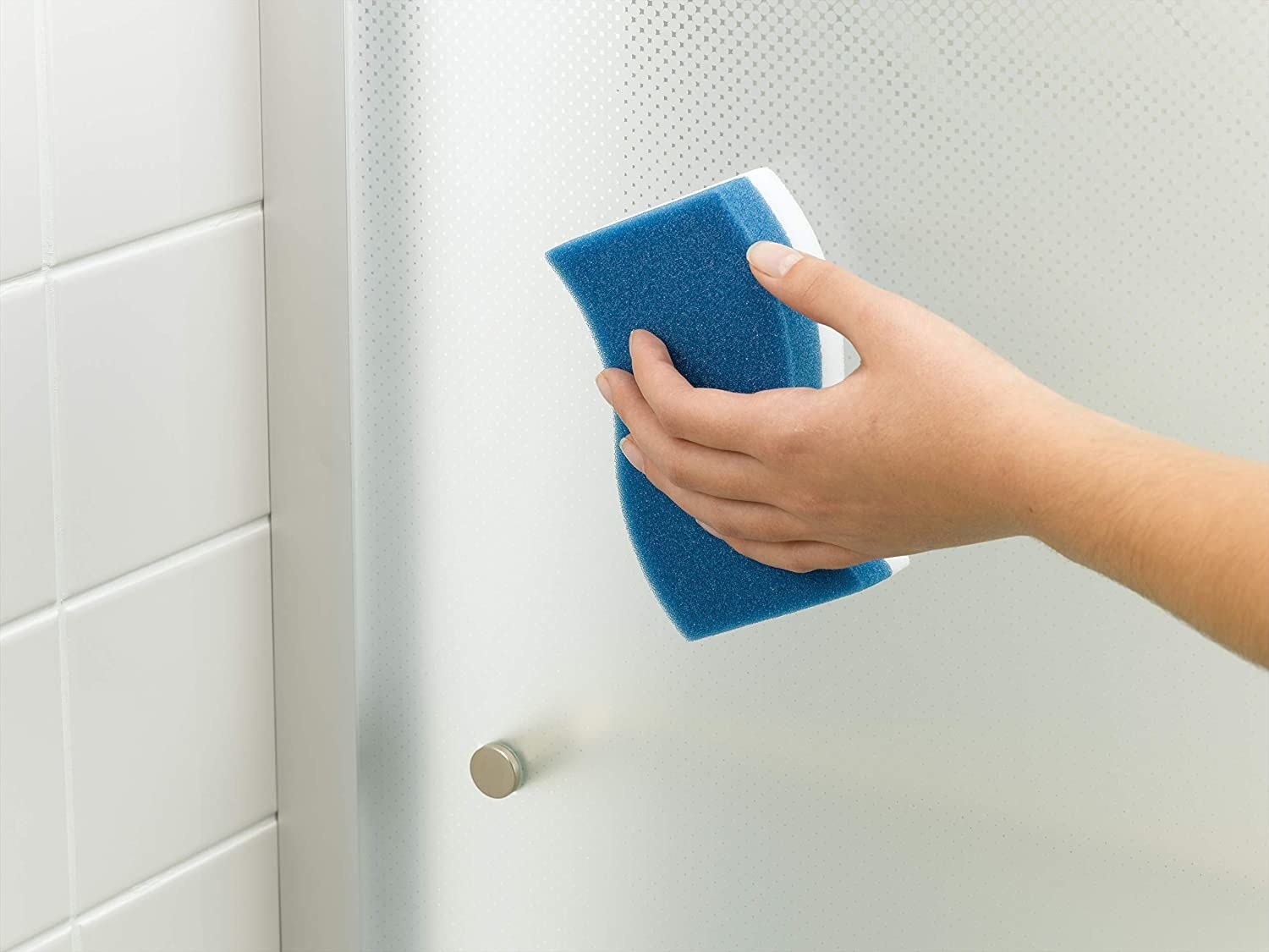 Model using the blue and white sided sponge to clean a shower door 