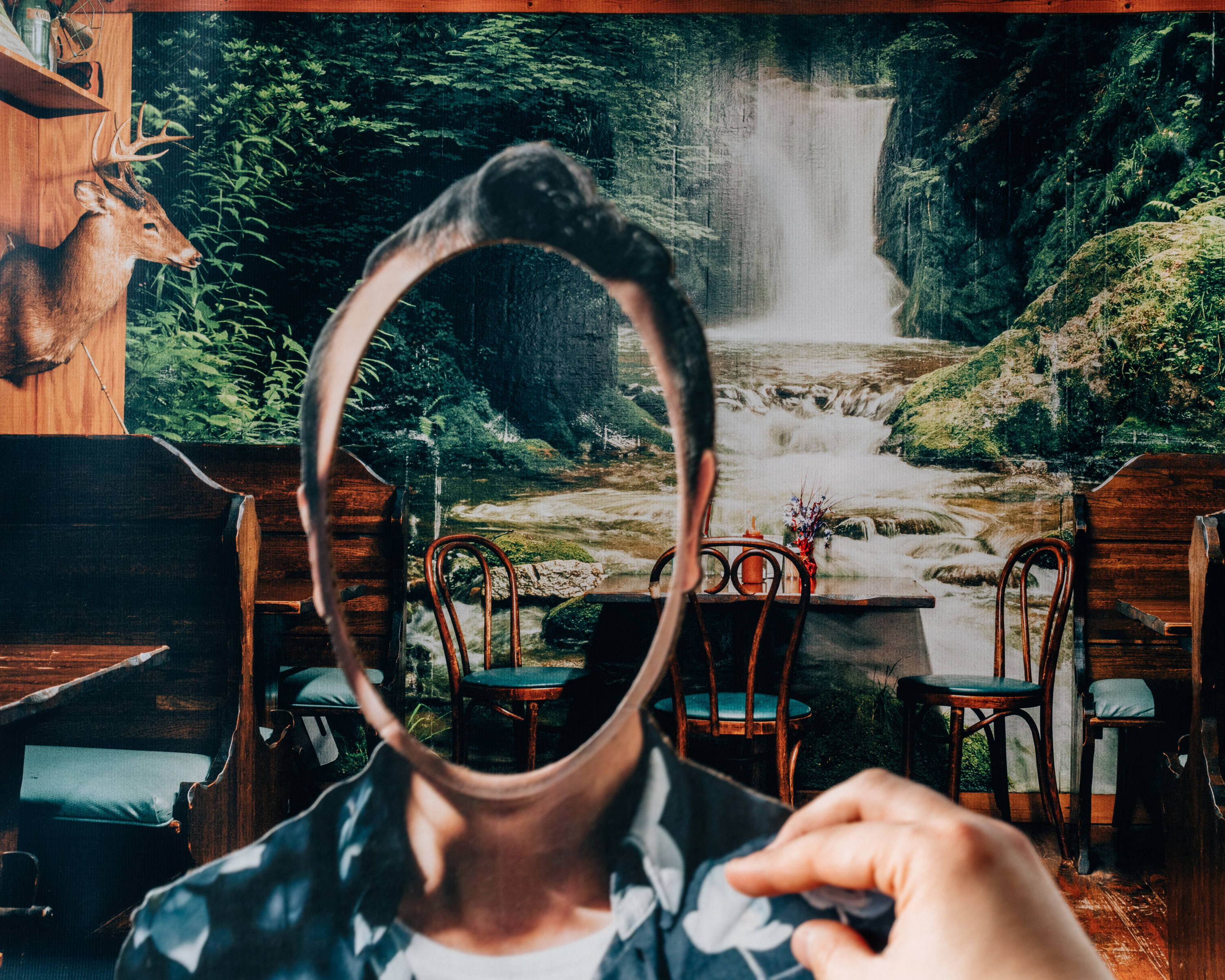 A photo collage shows someone&#x27;s hand on a person&#x27;s shoulder but with their face missing, revealing the background, a placid creek and waterfall scene, which appears to be wallpaper in a restaurant