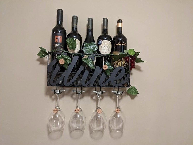 A metal wine container that reads &quot;wine&quot; mounted on a wall with clear wine glasses and faux ivy 