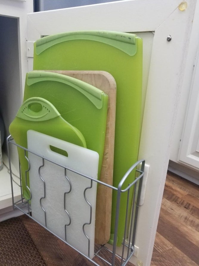 A silver over the wall organizer mounted on a cabinet door holding cutting boards