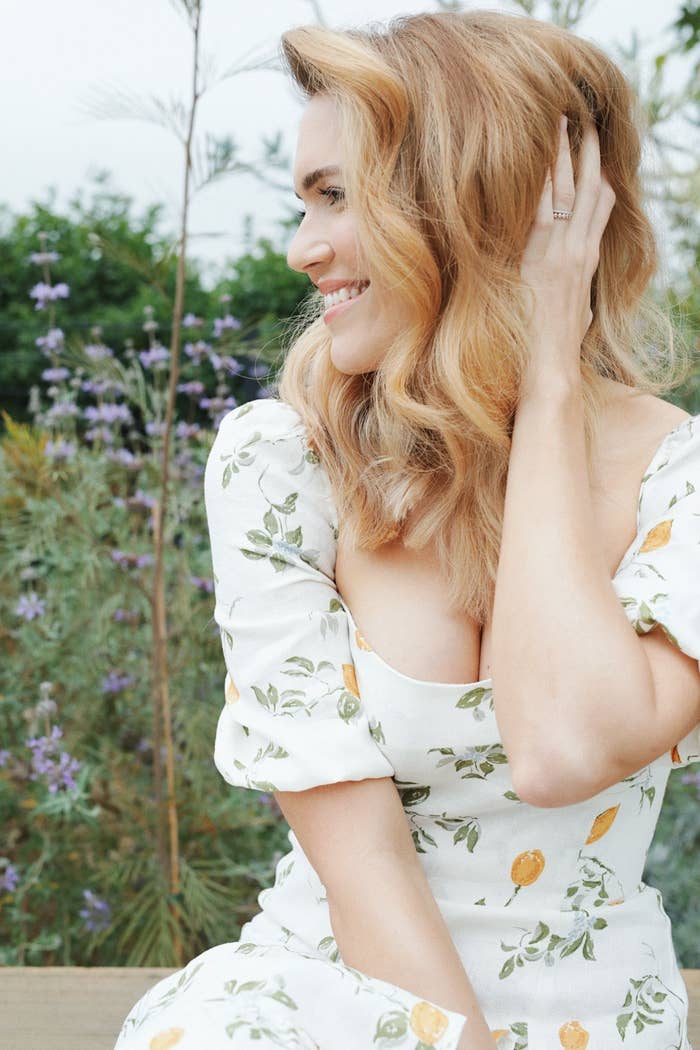 Mandy Moore with blonde hair, wearing a white sundress with citrus and flowers on it
