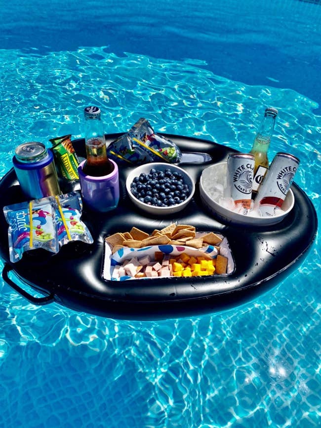 Black round inflatable holding a bucket of ice and three alcoholic drinks, snacks, cans of soda, Capri Suns, and more