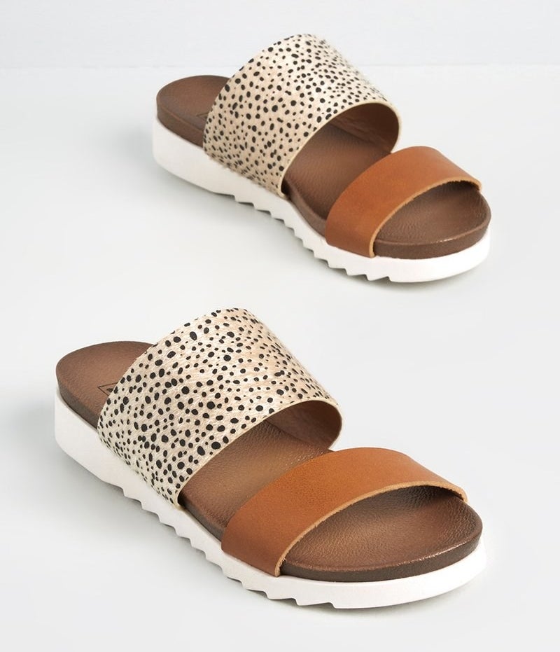 a pair of slide sandals with a plain brown strap, a black and tan printed strap, and a white lug sole 