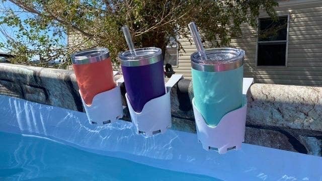 Three white cup holders clipped to the side of a pool