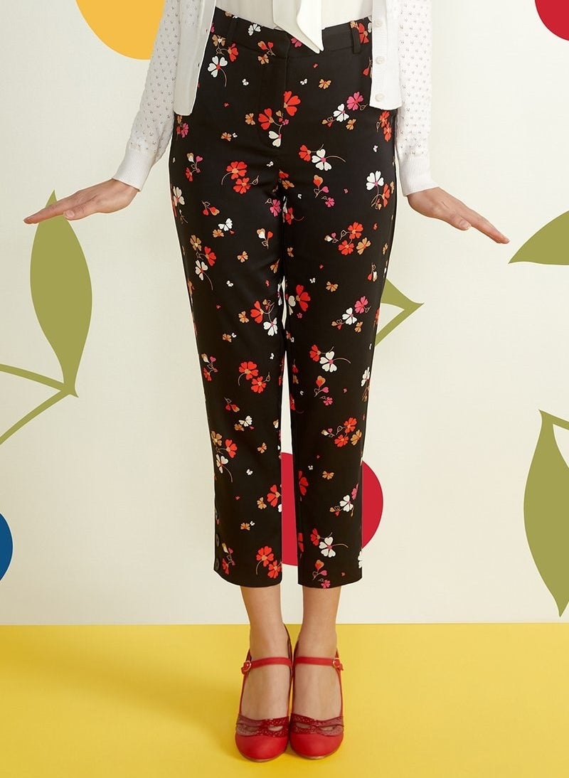 a model wearing a white top tucked into black tapered pants with a red, white and orange floral print 