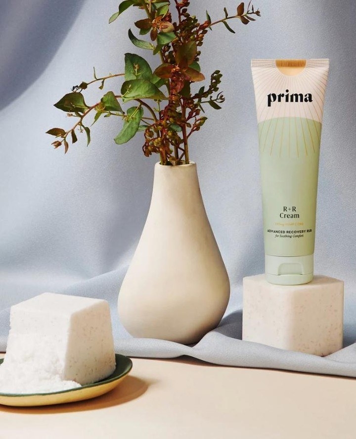 a product shot of the cream on top of a stone block next to a vase and we can see the size of the bottle which appears to be small but larger than mini size
