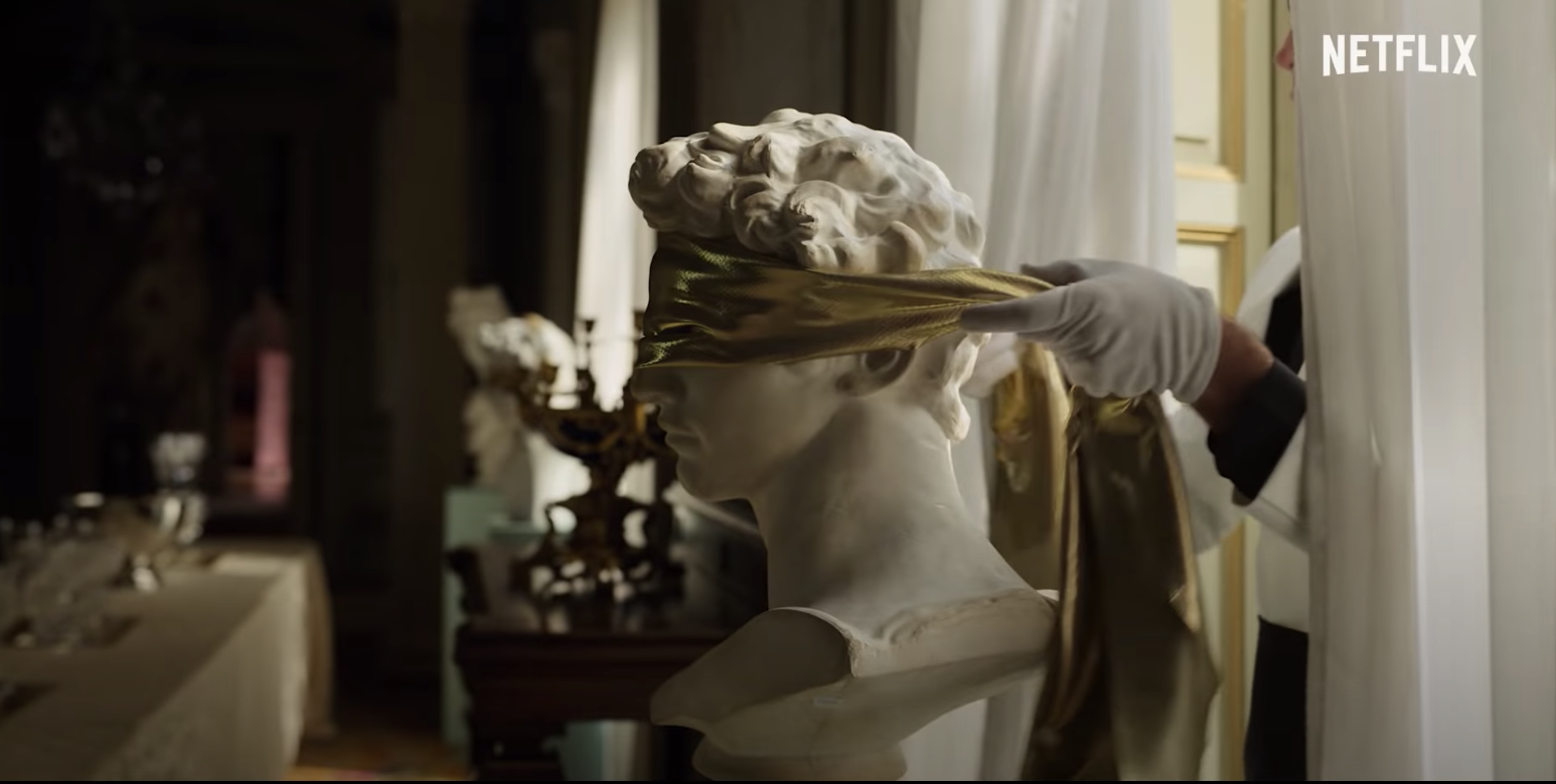 Someone placing a piece of cloth over the eyes of a bust