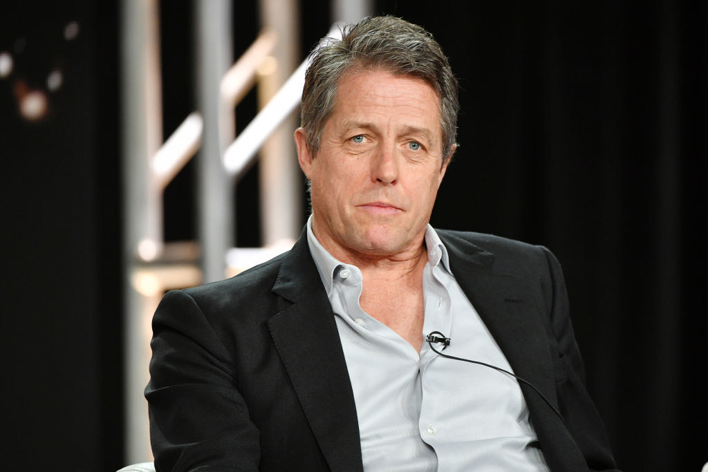 Hugh Grant with an open neck shirt and jacket, looking serious