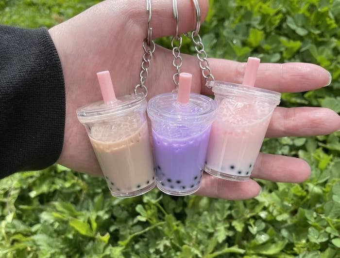 hand holding three boba keychains in pink, purple, and tan
