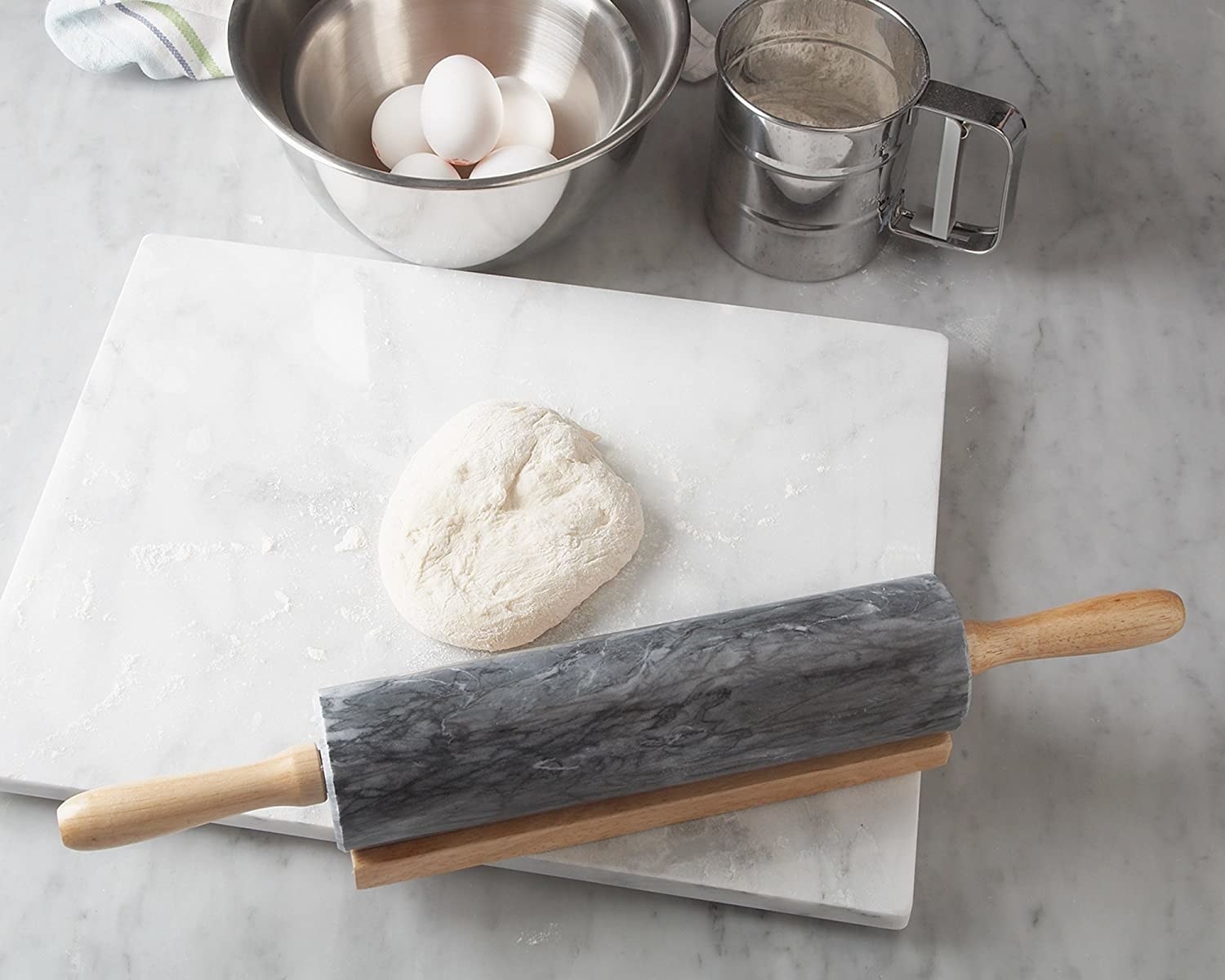 A marble rolling pin rolling out a ball of floured dough