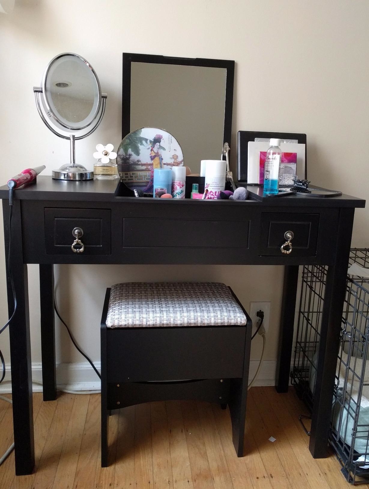 reviewer photo of a black vanity table with flip up mirror and products on top, with a stool tucked underneath