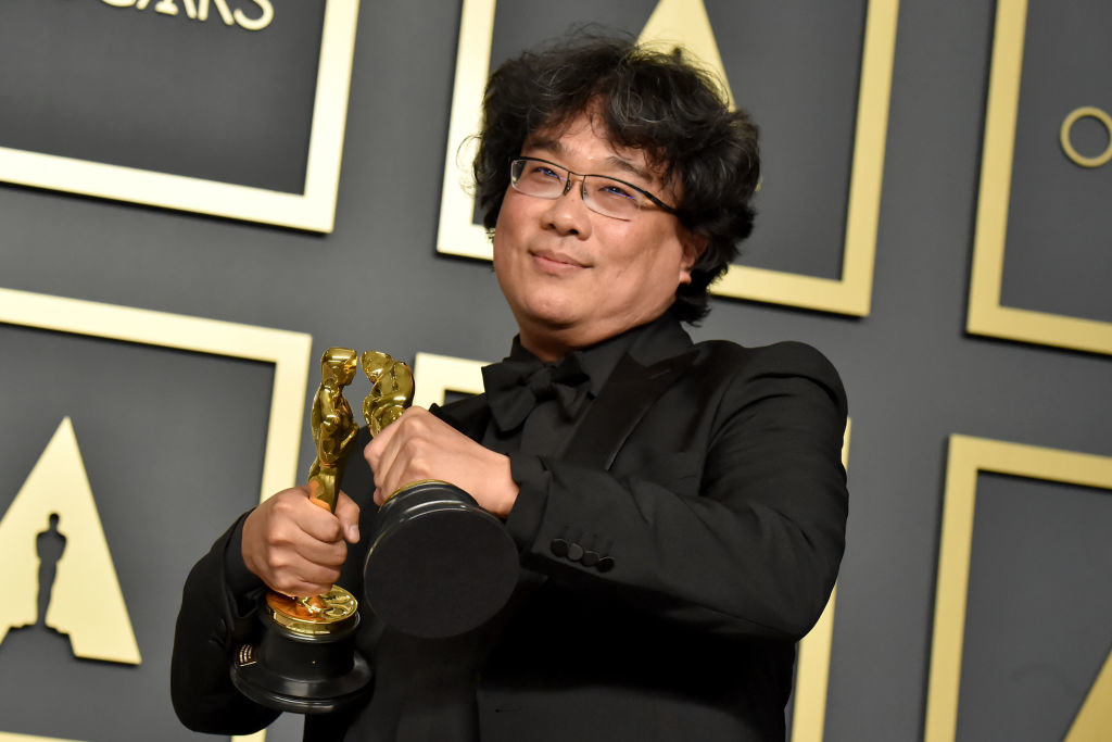 Parasite director Bong Joon-ho holding two of his four Oscar awards and making them kiss