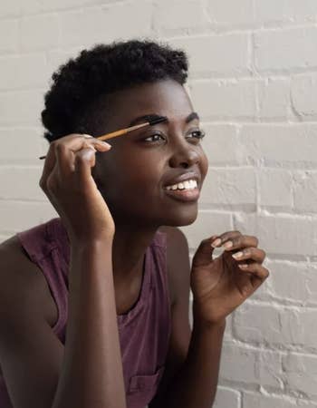 A model using a spoolie brush to apply oil to their eyebrows