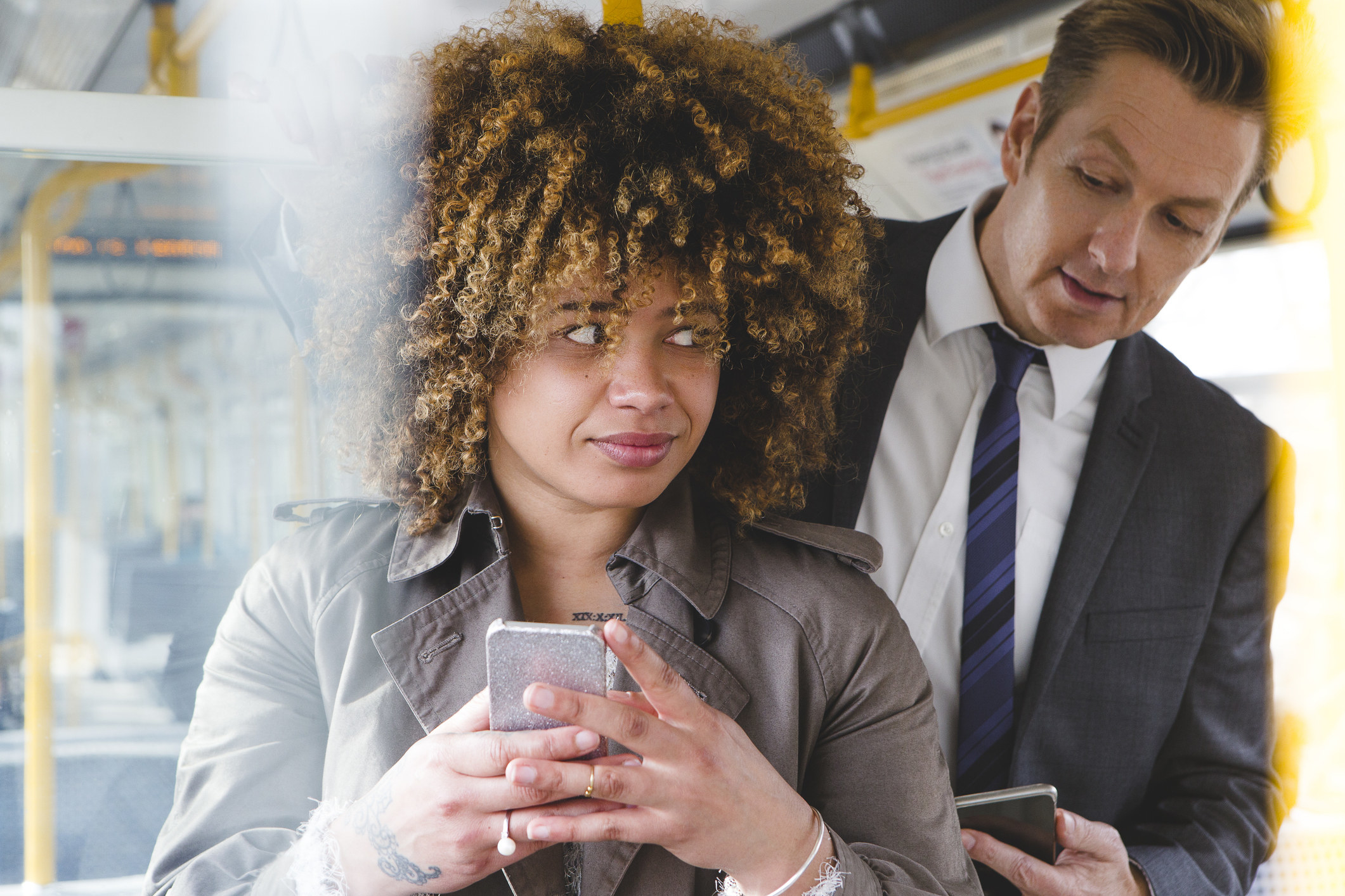 Man looking over a woman&#x27;s shoulder on the train at her phone screen.