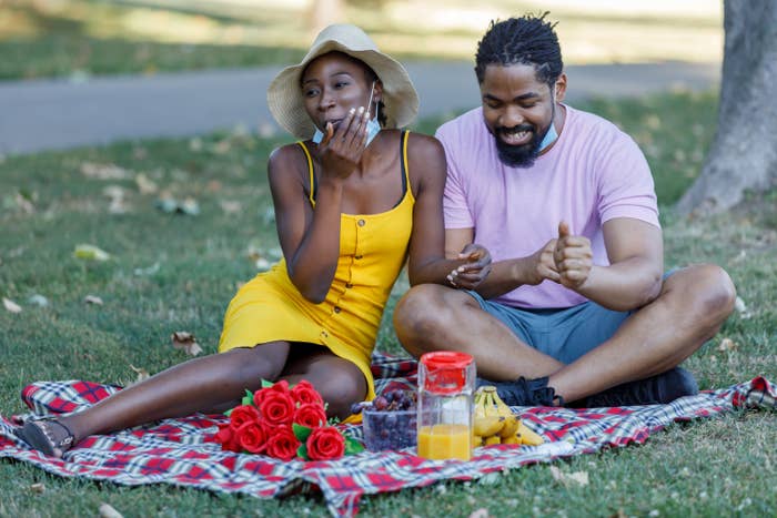 Two people on a date sit on a picnic blanket in a park