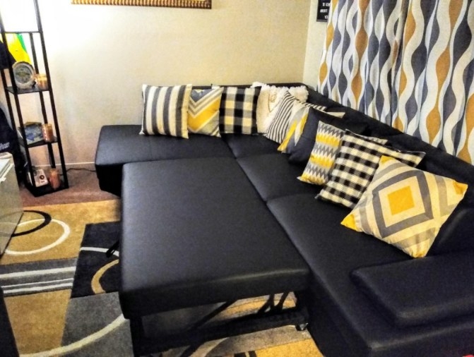 A reviewer’s image of a black sectional couch that is decorated with colorful pillows